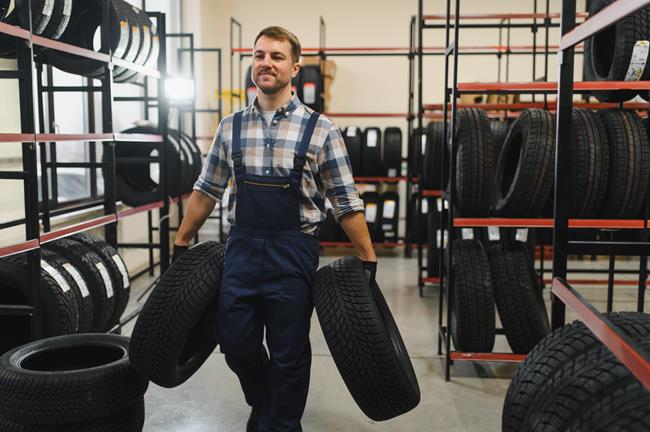 mechanik niosący w ręku opony samochodowe