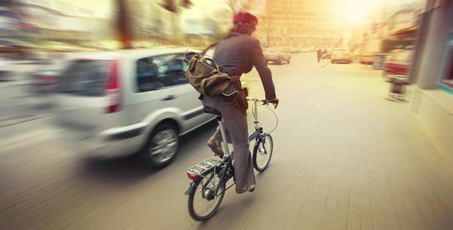 Rowerzysta poruszający się w ruchu miejskim. Obok przejeżdża samochód osobowy