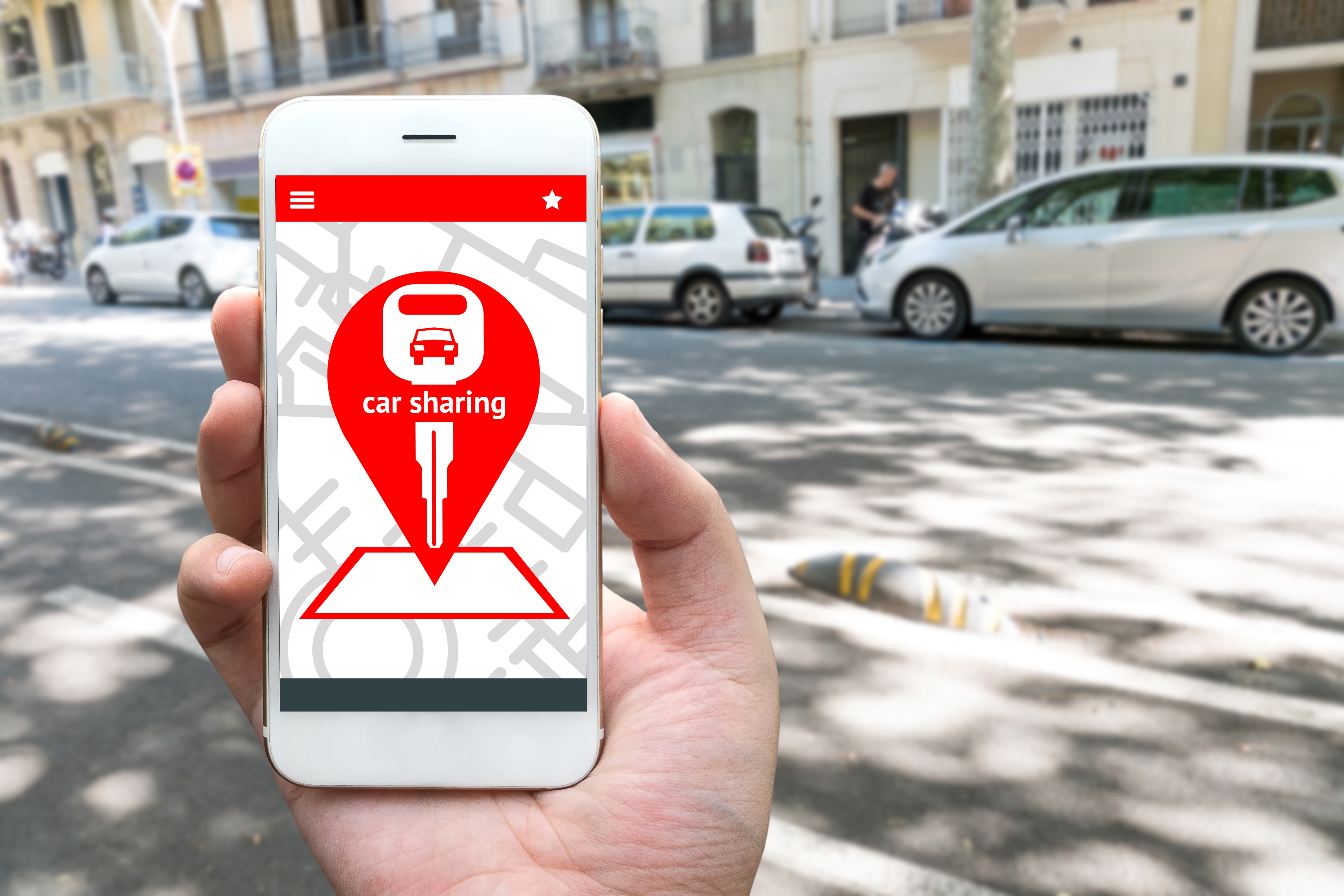 Telefon ze znaczkiem car sharing, w tle ulica i zaparkowane samochody