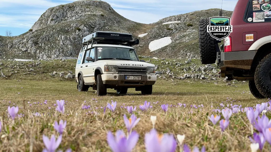 ujęcie z ziemi na biały Land Rover 4x4 i kawałek bordowego auta terenowego