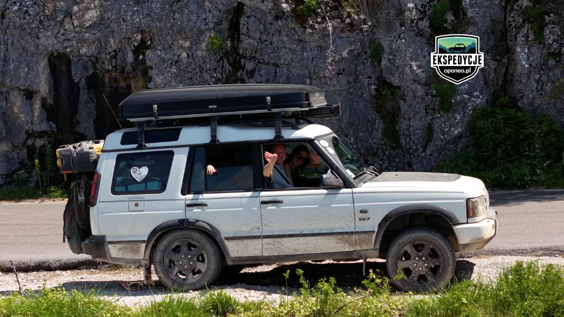 biały Land Rover z pasażerami machającycmi z okien