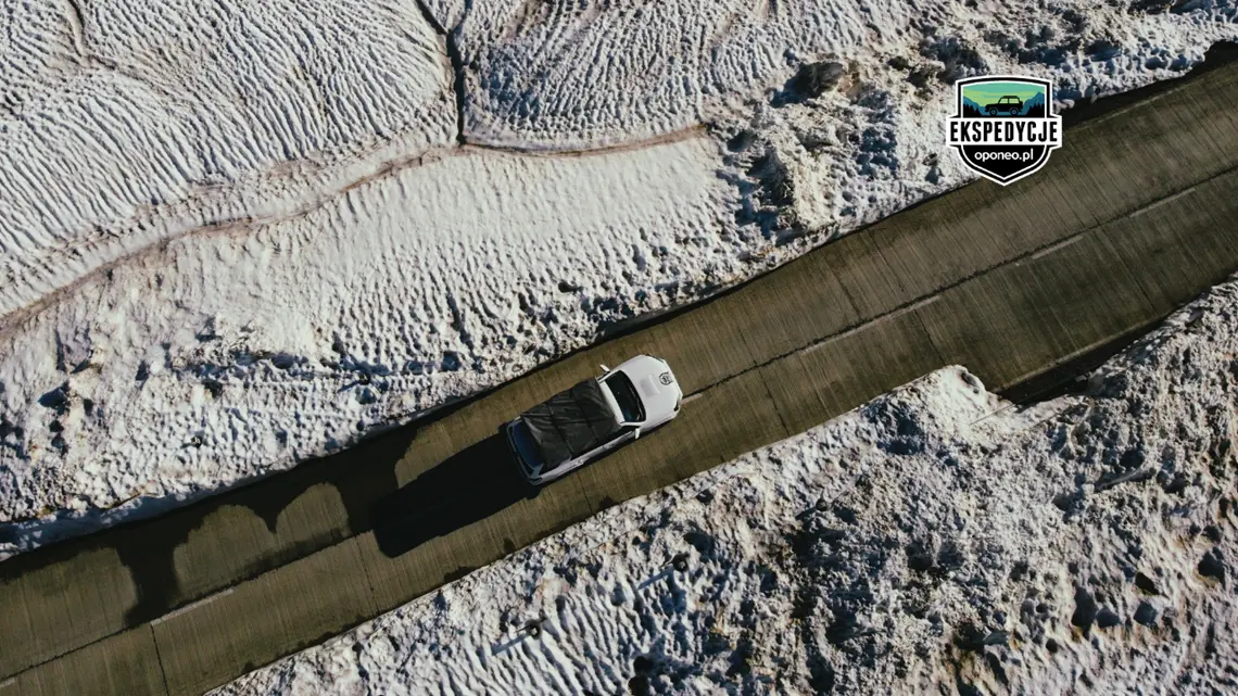 białe auto 4x4 z lotu ptaka na asfaltowej drodze wokół ośnieżononej przełęczy